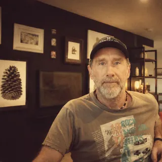 Andrew Farran in his studio, in front of a wall of framed prints.